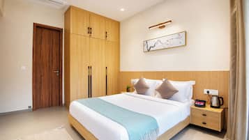 A hotel room with a large bed, a wooden wardrobe, a bedside table with a kettle, and a wall-mounted artwork.