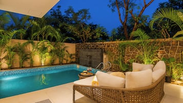 A poolside area with a wicker sofa, a stone wall, and tropical plants.