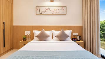 Ein Hotelzimmer mit einem großen Bett, zwei Kissen, einem Nachttisch mit Wasserkocher, einer kleinen Pflanze und einer Wandleuchte.