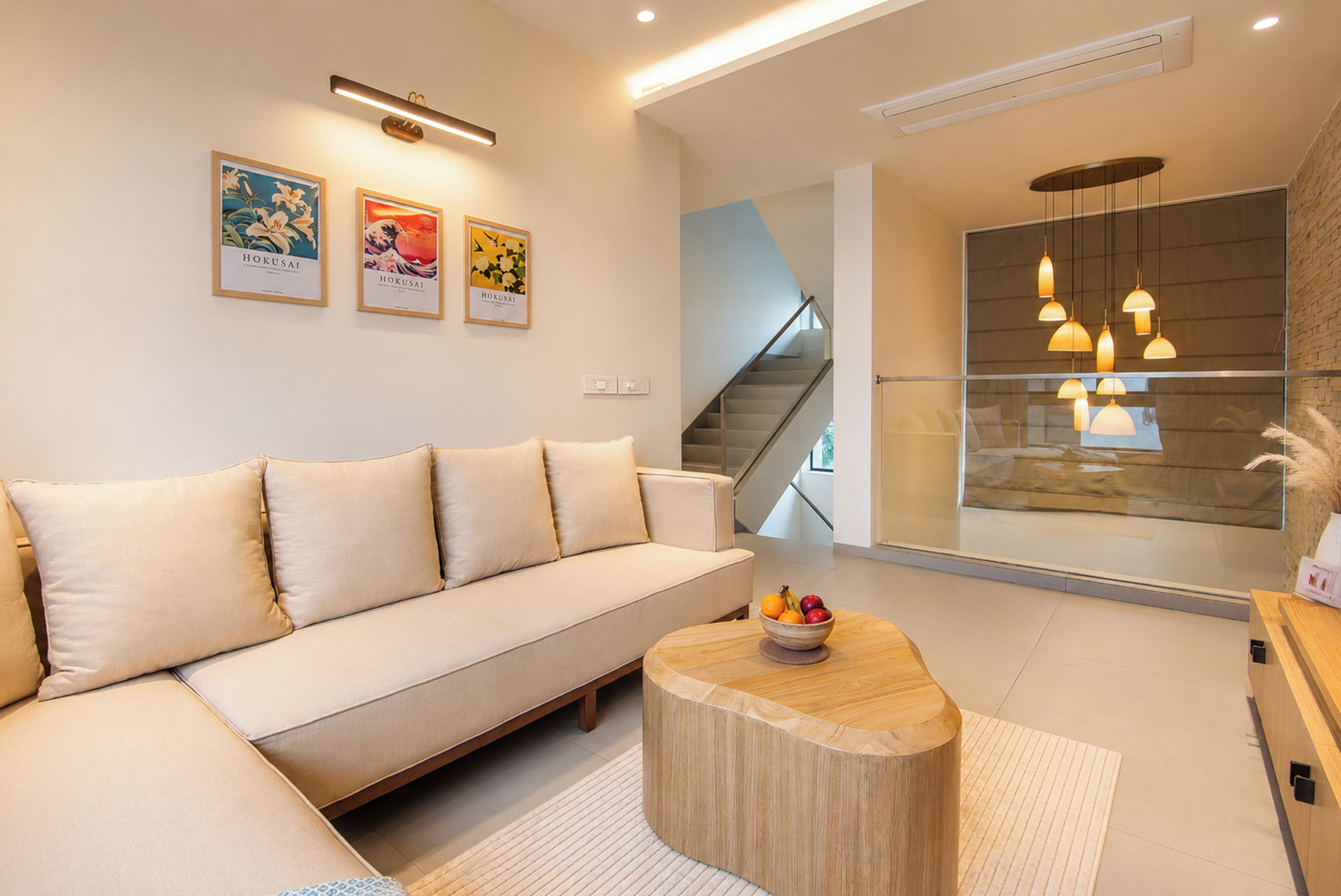 A modern living room with a sofa, a wooden coffee table with fruit, and a staircase leading to an upper level.