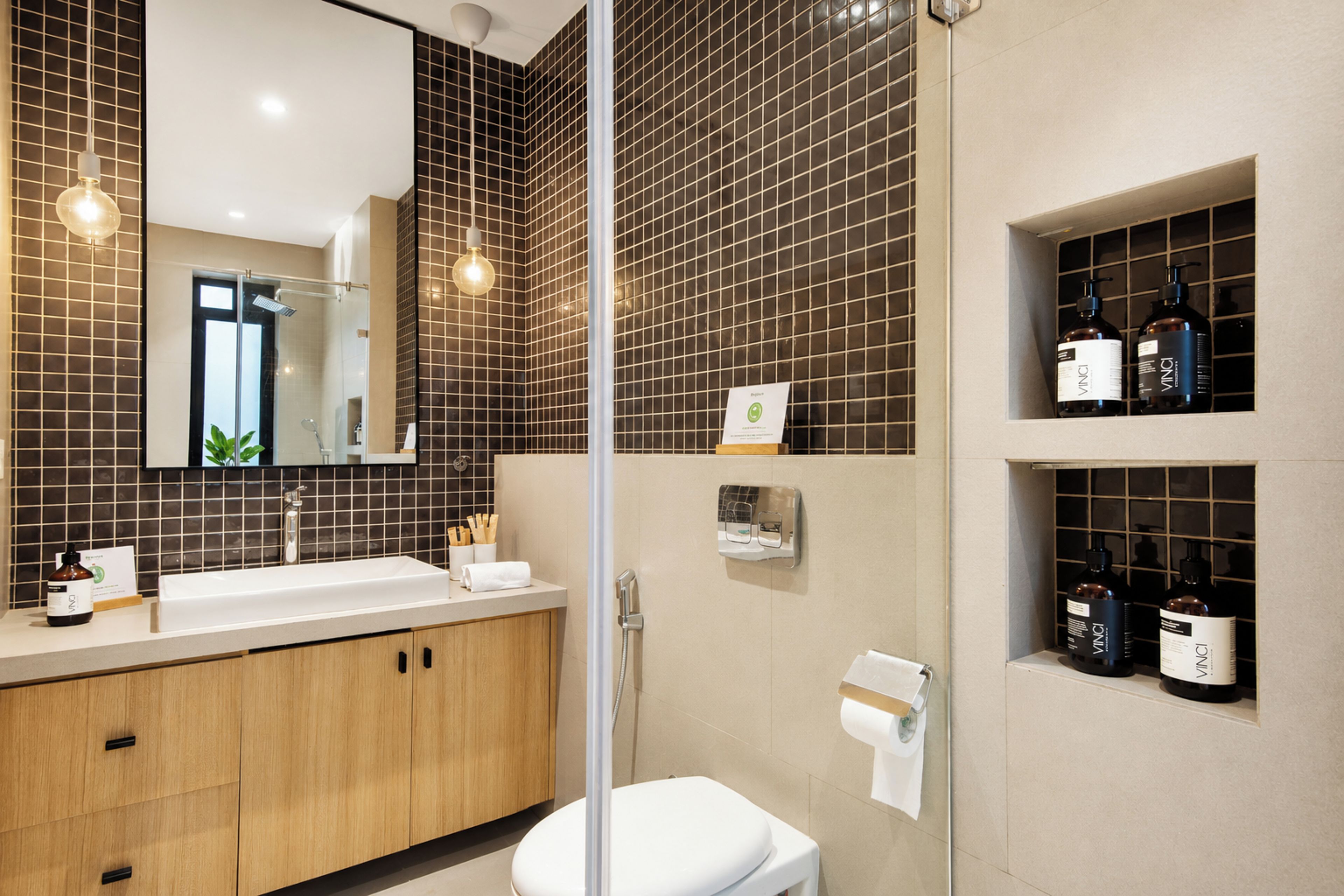A modern bathroom with a large mirror, a shower, and a toilet. There are shelves with toiletries and a towel rack.
