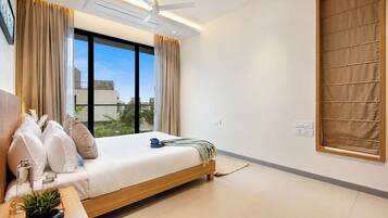 Een moderne slaapkamer met een bed, gordijnen, een plafondventilator en uitzicht op gebouwen.