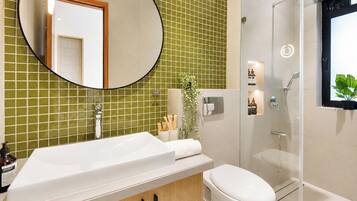 A bathroom with a white sink, toilet, and shower. There is a mirror above the sink and a green tiled wall.