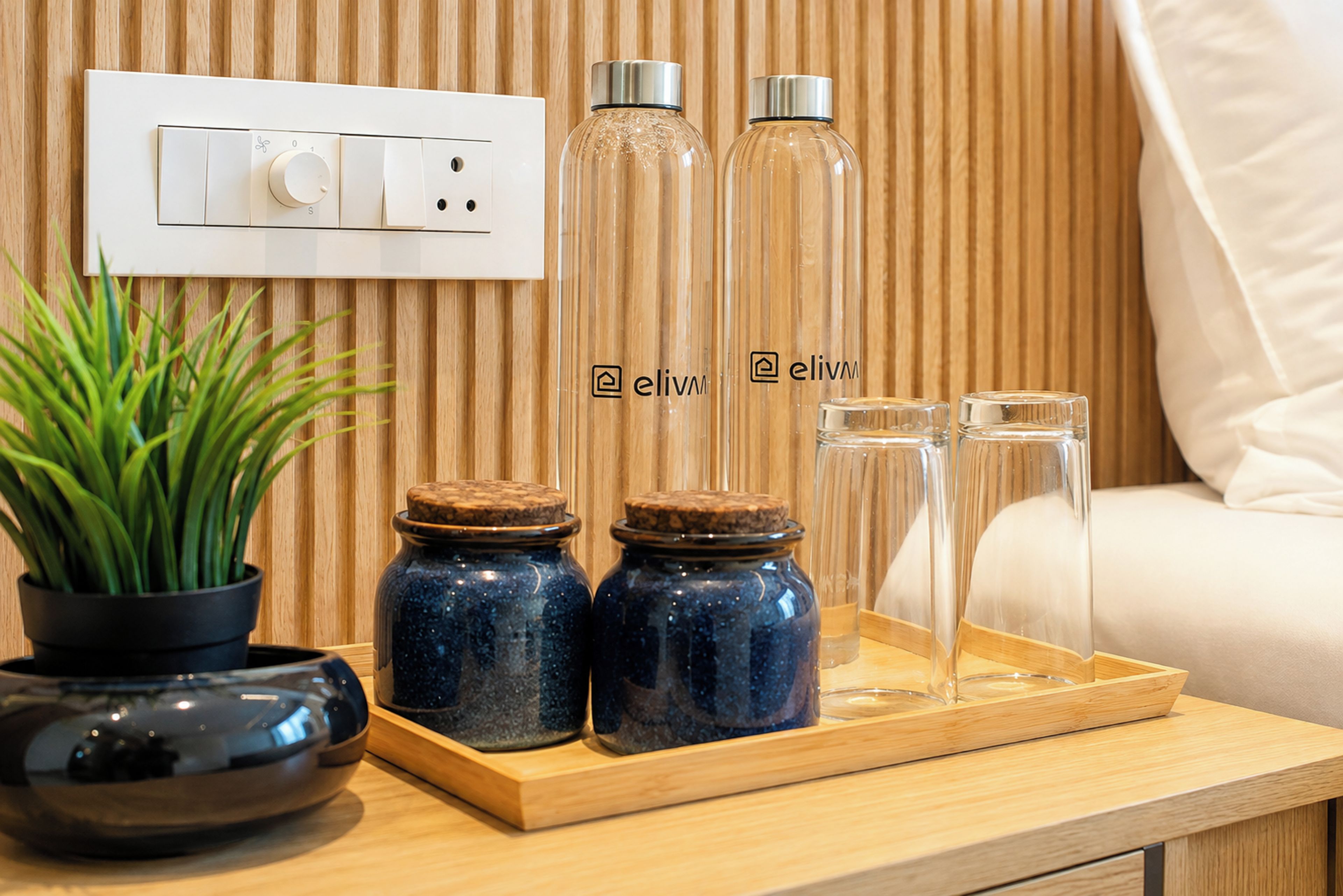 A wooden tray with jars and glasses, a potted plant, and a wall socket.