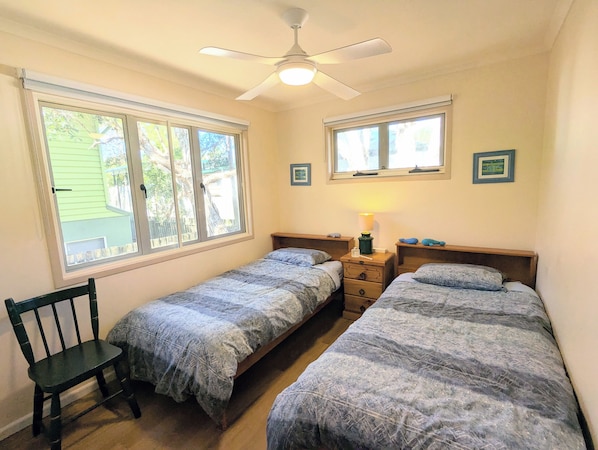 Une chambre avec deux lits simples, une chaise, une table de chevet avec une lampe et un ventilateur de plafond.