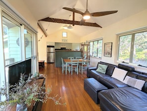 A spacious living area with a dark leather sofa, wooden dining table, and a kitchen in the background. - Heather Beach House - Three Sisters (Point Lookout)