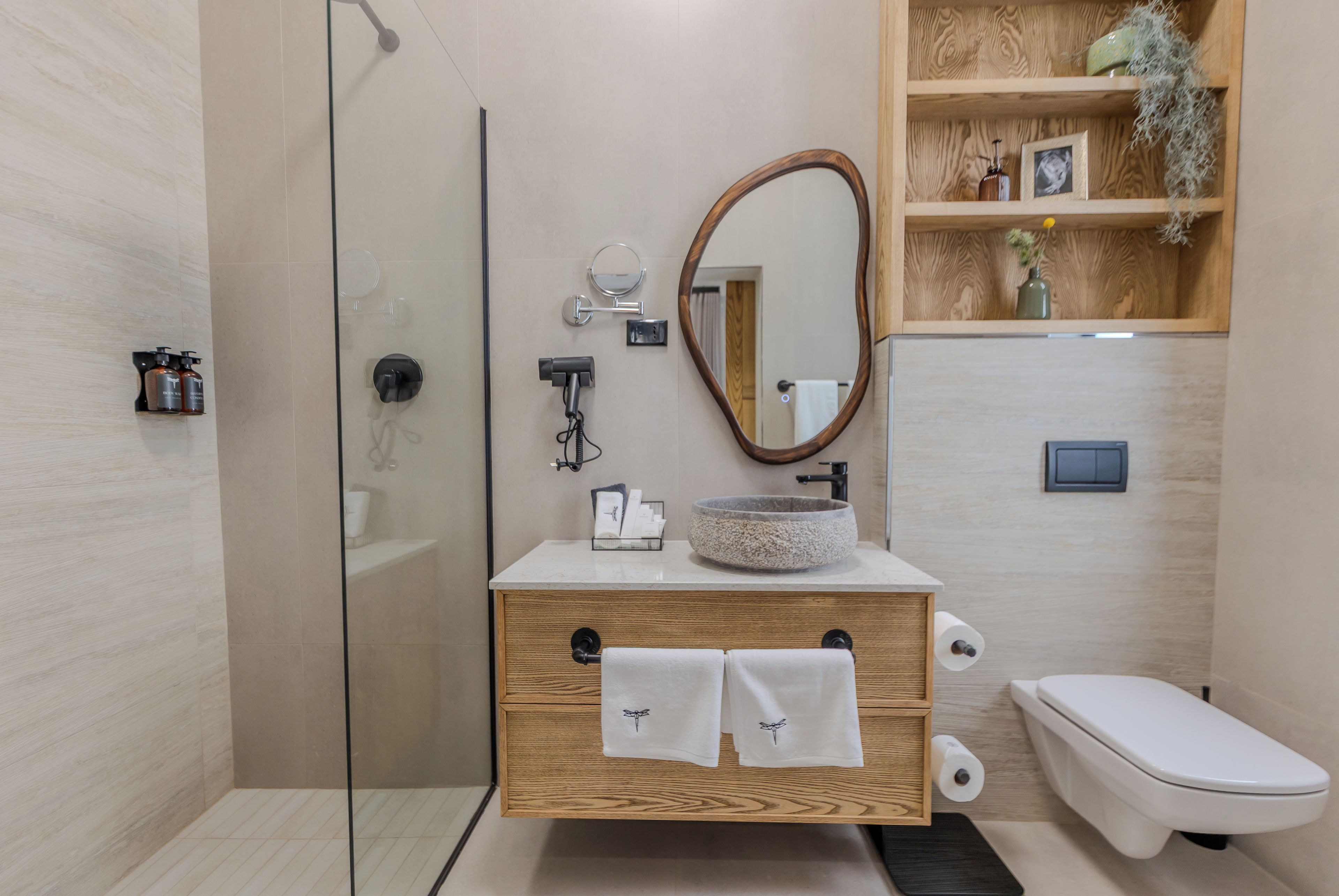 A modern bathroom with a glass shower enclosure, a wooden vanity with a stone sink, and a toilet.