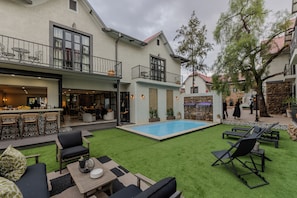A courtyard with a swimming pool, outdoor seating, and a bar area. - Gracious Whisp Boutique Hotels (Windhoek)