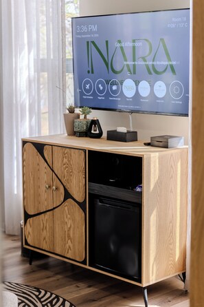 Una habitación de hotel con un armario de madera, un televisor mostrando una interfaz digital y una planta pequeña en maceta sobre el mueble.