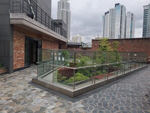 A rooftop terrace with a glass balustrade, stone flooring, and a view of high-rise buildings in the background. - Dae Sung Gwan Onchun Hotel (Busan)