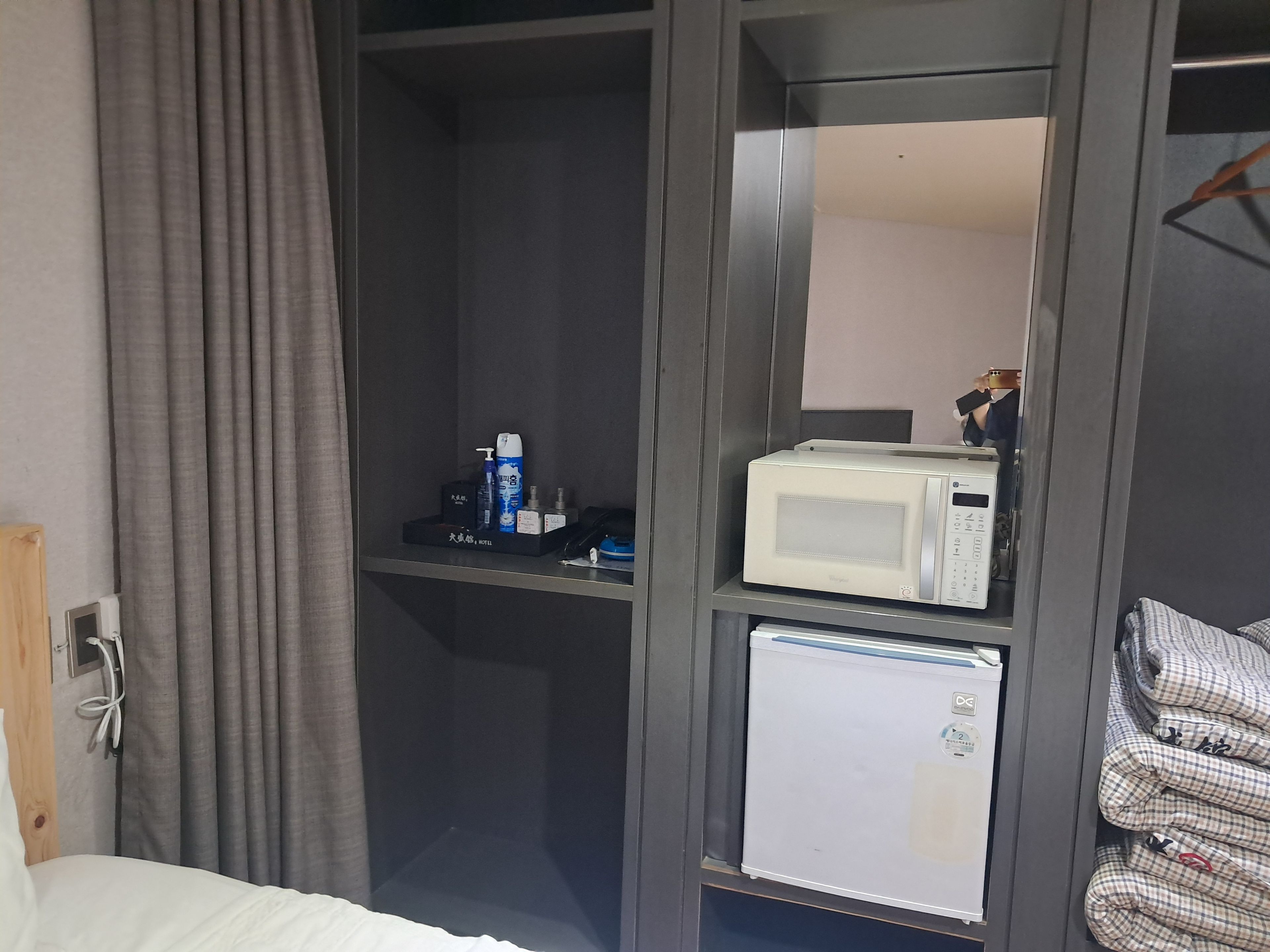 Habitación de hotel con cama, refrigerador pequeño, microondas y estante con artículos de tocador.