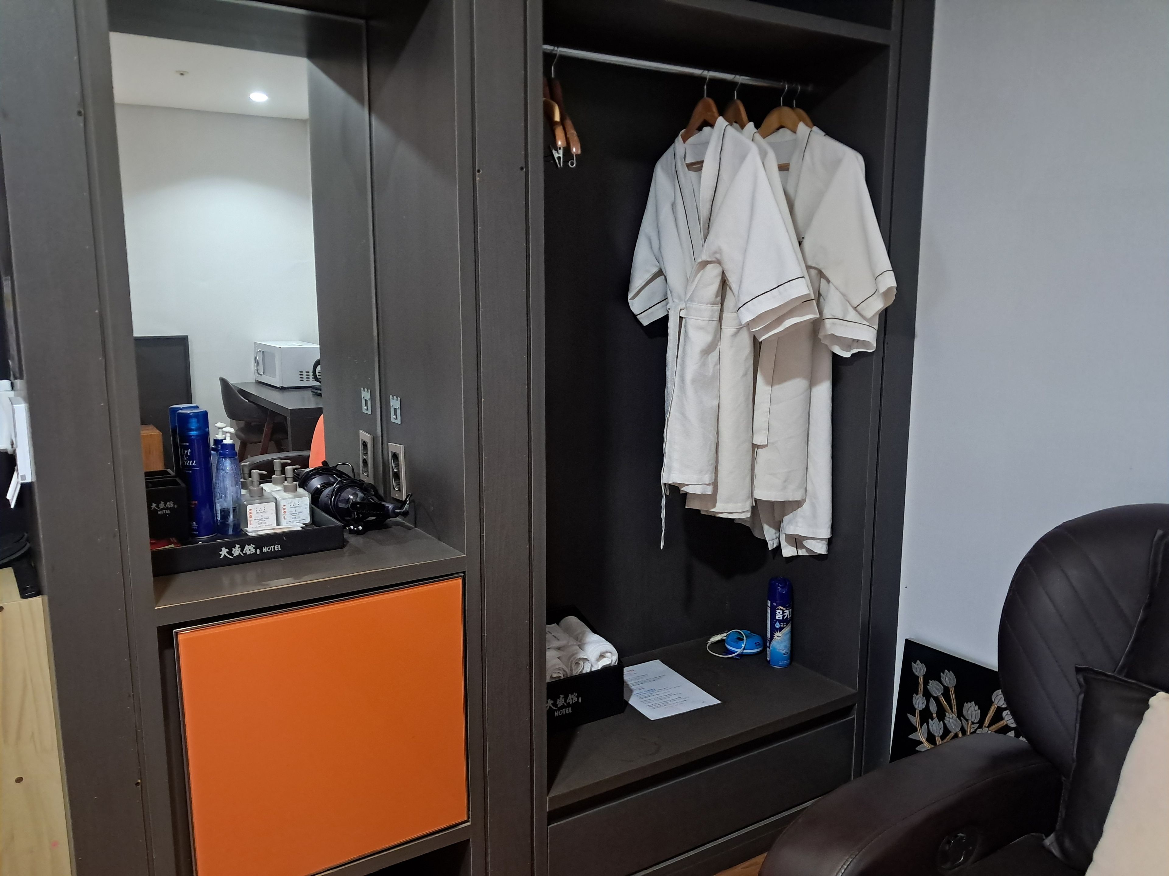 Camera d'albergo con armadio contenente uno specchio, una scrivania con articoli da toilette e una sedia.