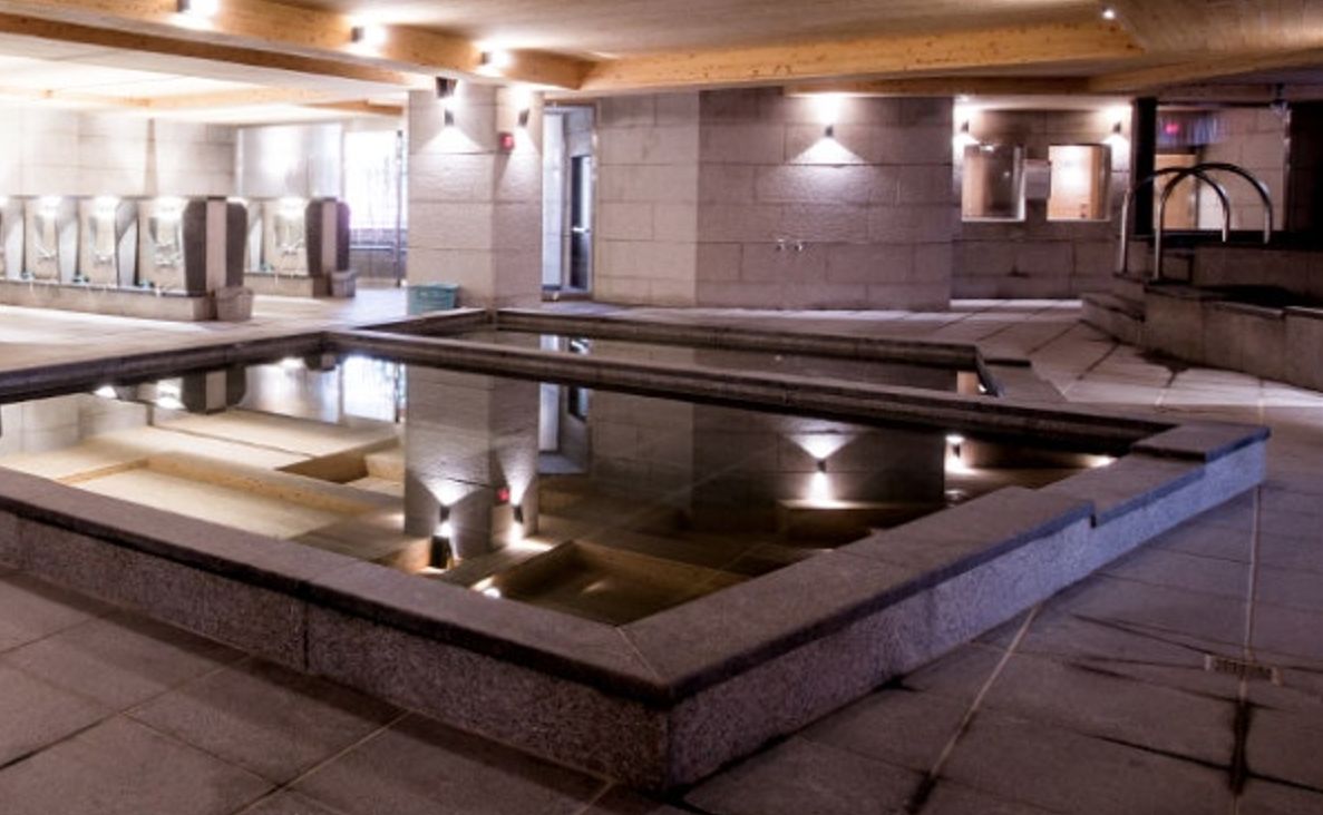 A large indoor pool with clear water, surrounded by stone walls and wooden beams.