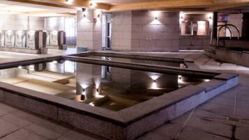 A large indoor pool with clear water, surrounded by stone walls and wooden beams.