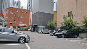Parkkipaikka, jossa on useita autoja, rakennus, jossa on kyltti, ja korkea pilvenpiirtäjä taustalla.