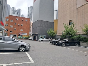 A parking lot with multiple cars, a building with a sign, and a tall skyscraper in the background. - Dae Sung Gwan Onchun Hotel (Busan)