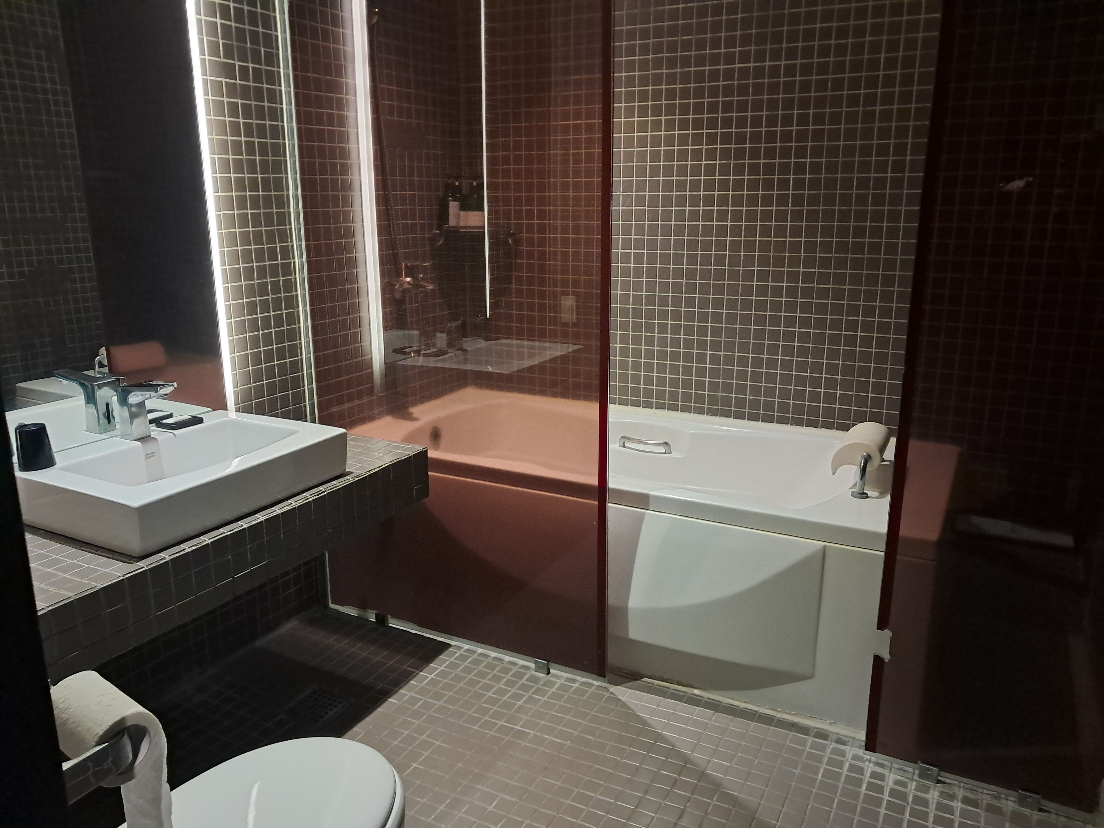A modern bathroom with a large mirror, a white sink, a bathtub, and a toilet.