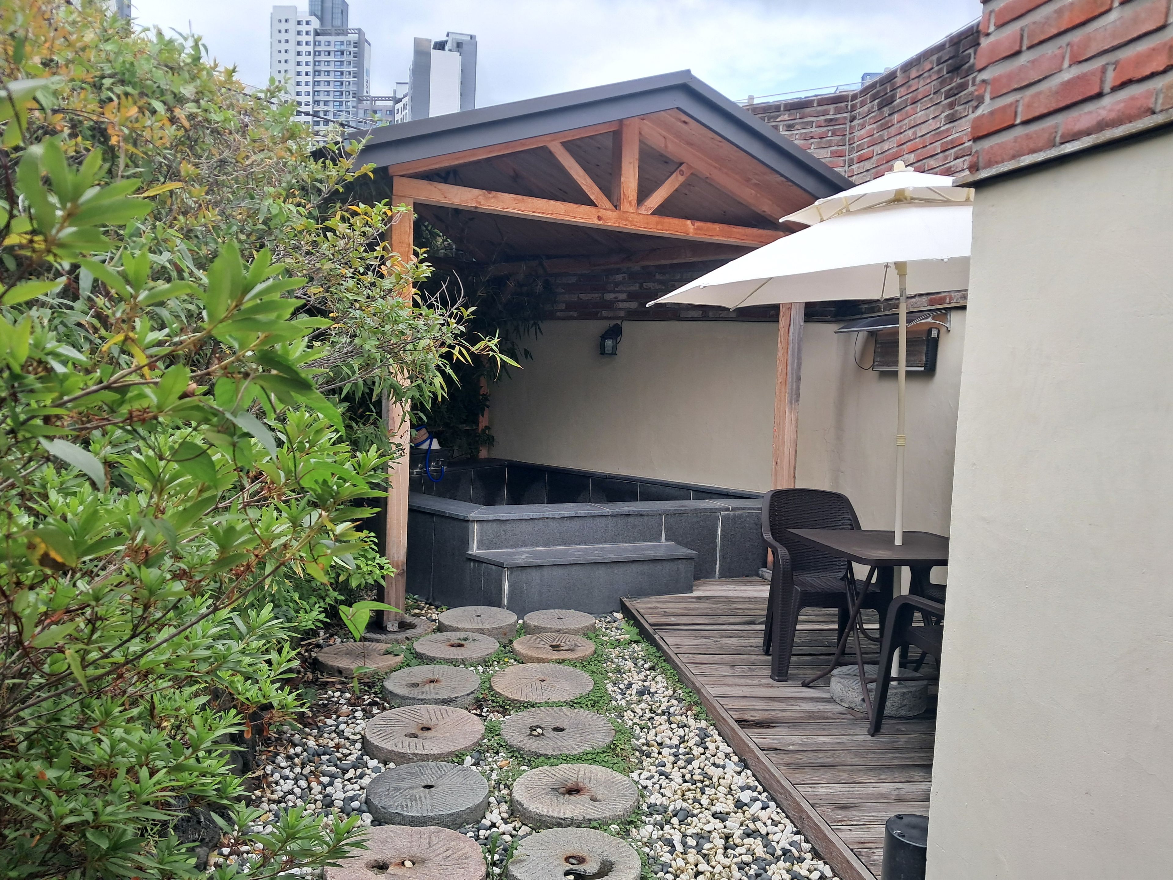 A rooftop patio with a wooden pergola, a hot tub, and a table with chairs.
