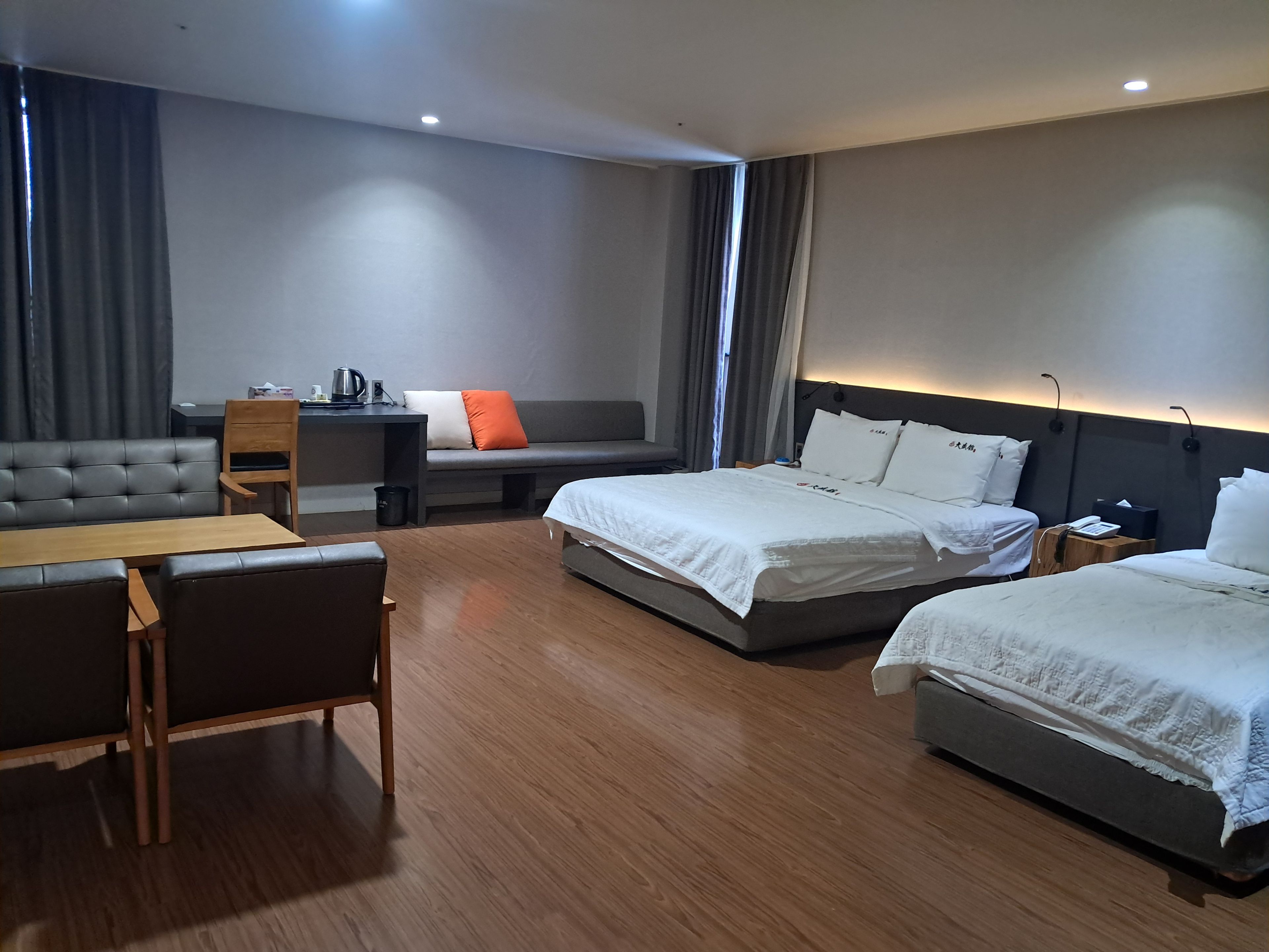 A hotel room with a sofa, two beds, a desk, and a small table.