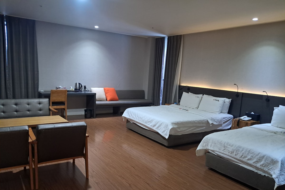 A hotel room with a sofa, two beds, a desk, and a small table.