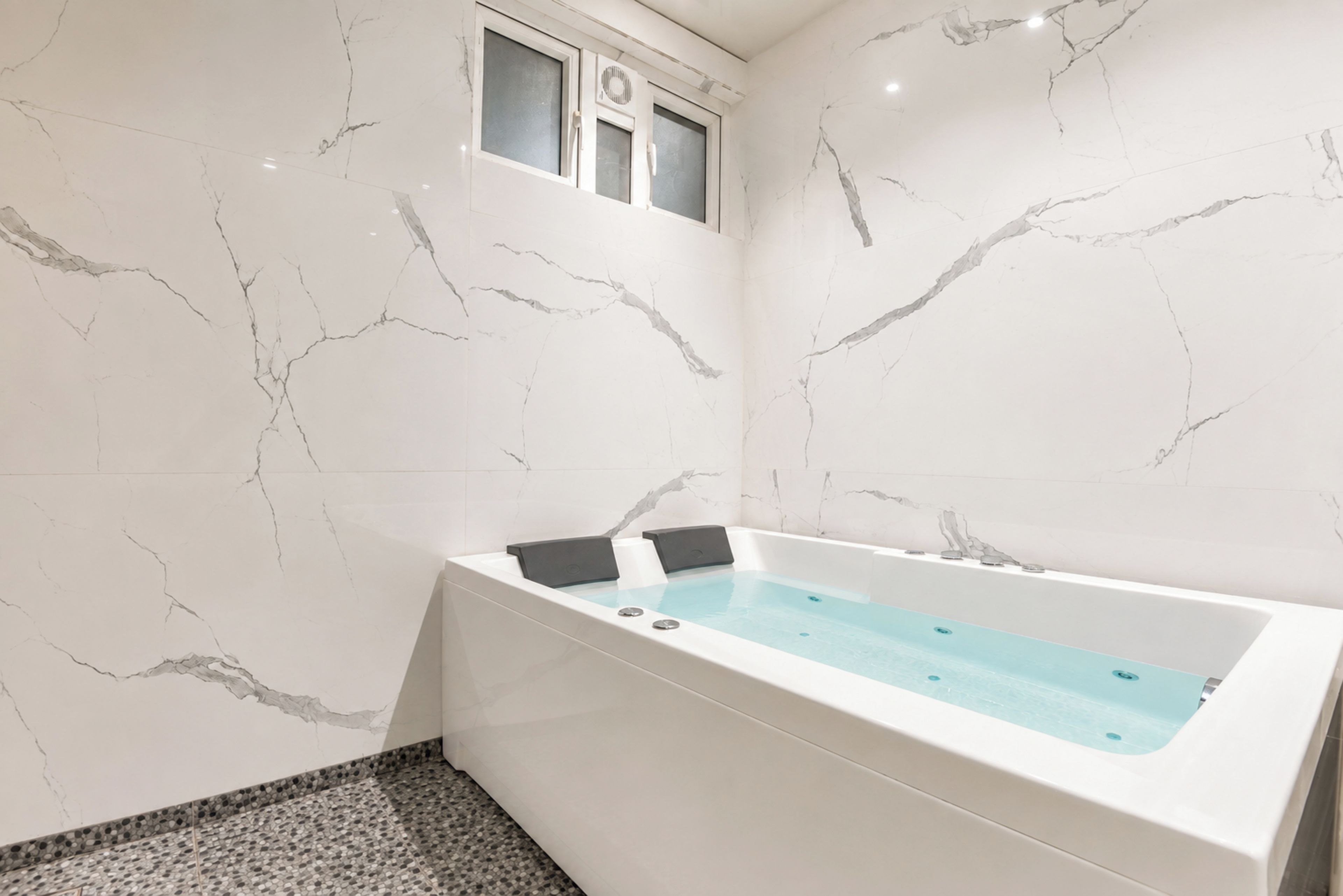 A modern bathroom with a marble wall, a bathtub, and a small window.