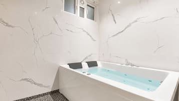 A modern bathroom with a marble wall, a bathtub, and a small window.