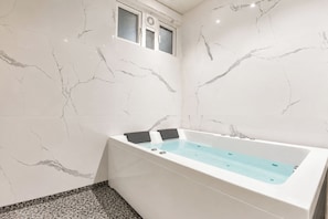 Een moderne badkamer met een marmeren wand, een badkuip en een klein raam.