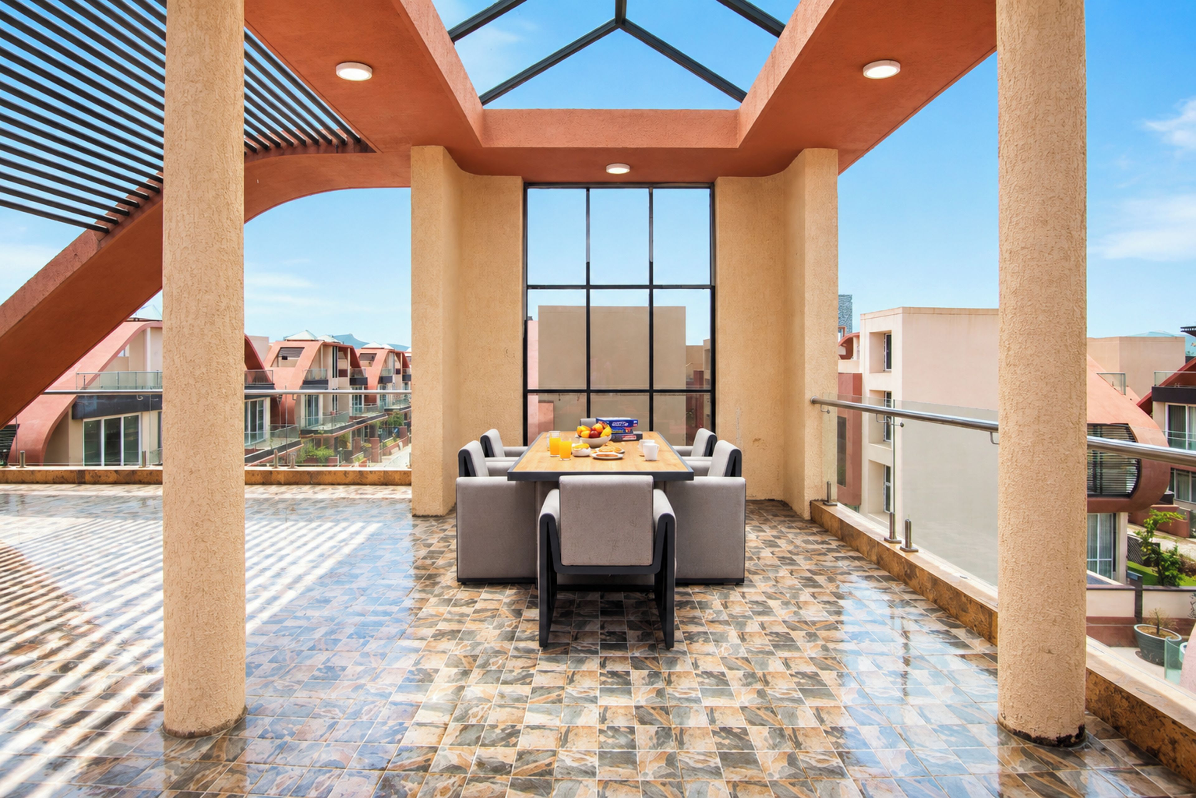 A covered outdoor dining area with a table and chairs, a tiled floor, and a view of surrounding buildings.