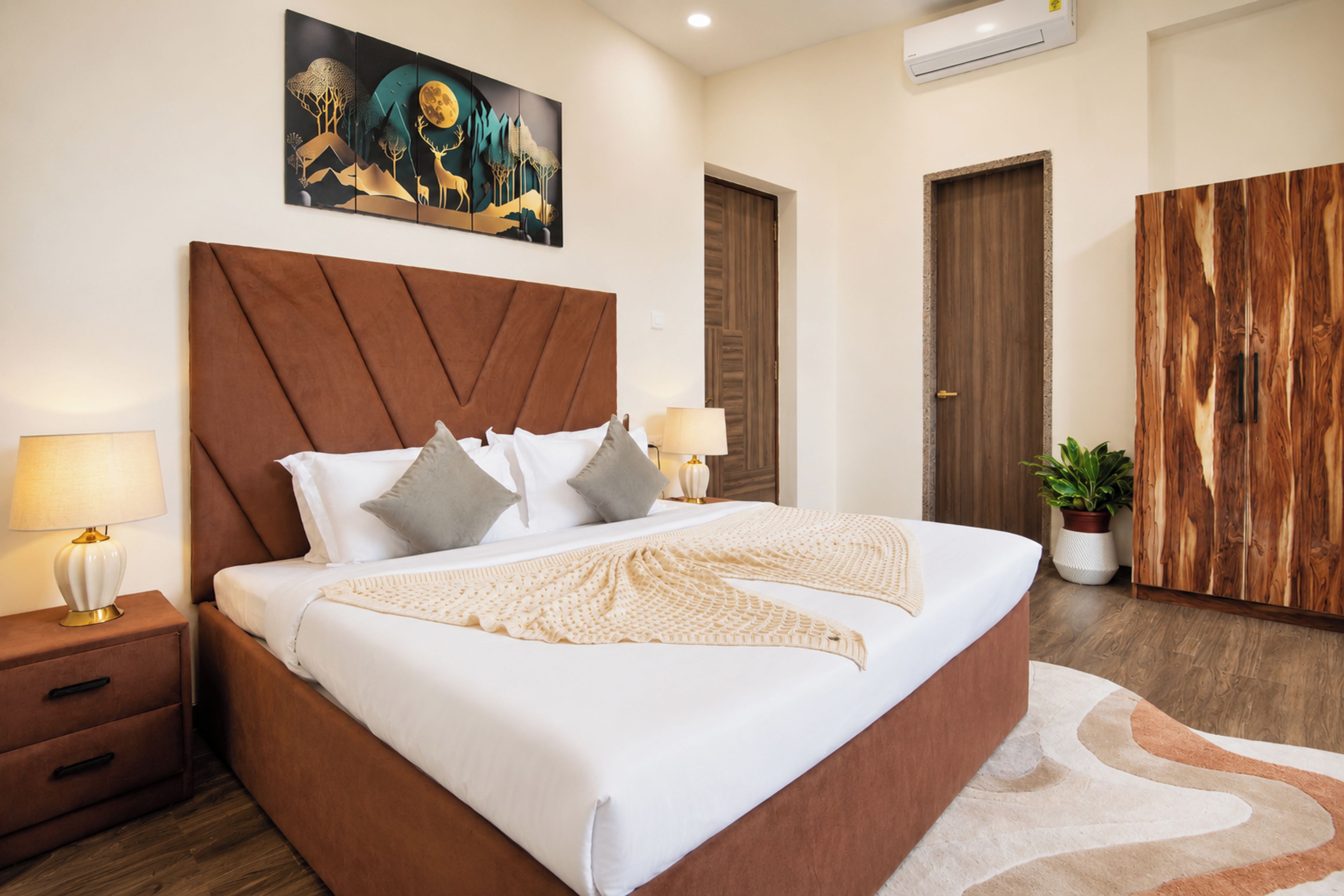A modern bedroom with a large bed, bedside lamps, a painting above the bed, and a wardrobe.