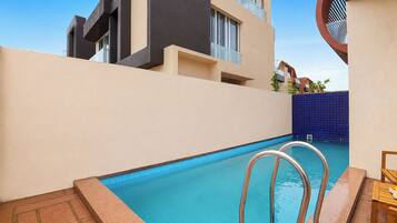 A swimming pool with metal ladders, a tiled deck, and a building with balconies in the background.