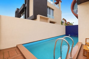 A swimming pool with metal ladders, a tiled deck, and a building with balconies in the background. - ELIVAAS signature Eulophia 3BHK Villa (Varsoli)