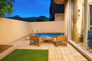 Área na piscina com mesa e cadeiras, porta de vidro que dá para uma varanda e vista para montanhas ao fundo.
