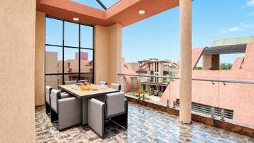 A rooftop terrace with a dining table and chairs, a view of the cityscape, and a tiled floor.