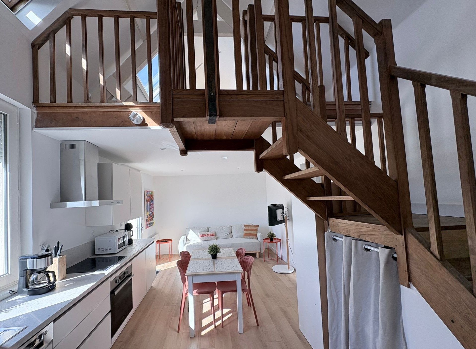 A modern kitchen with a dining area, wooden staircase, and a small balcony.
