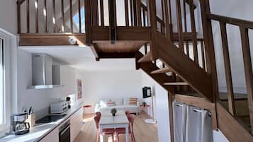 A modern kitchen with a dining area, wooden staircase, and a small balcony.