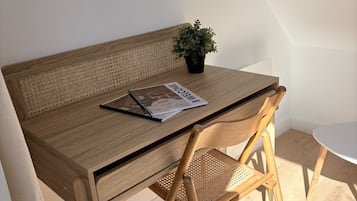 A wooden desk with a woven chair, a small potted plant, and a magazine on the table.