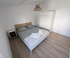Une chambre à coucher comprenant un lit, des tables de chevet, une armoire et un luminaire suspendu.