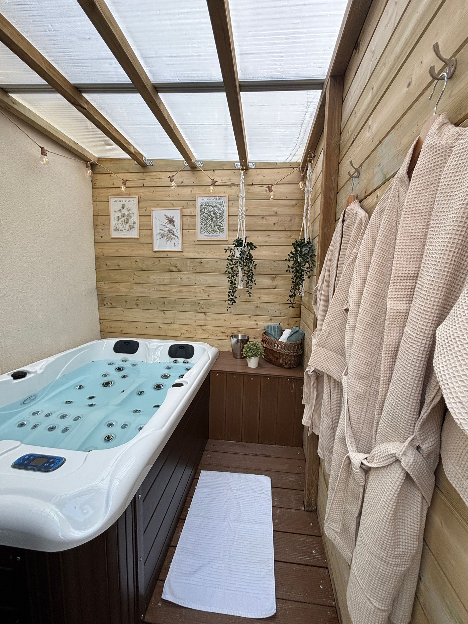 Een houten wellnessruimte met een jacuzzi, handdoeken en ingelijste botanische prints op de muur.