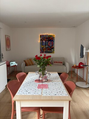 Een eetgedeelte met een tafel voor vier personen, omringd door rode stoelen, een vaas met rode rozen en een aan de muur bevestigd kunstwerk.