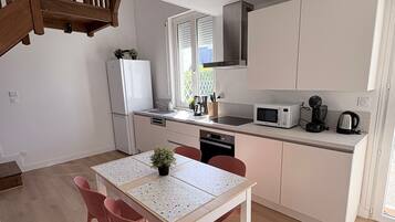 A modern kitchen with white cabinets, a microwave, and a coffee maker. There is a dining table with chairs and a staircase leading to another level.