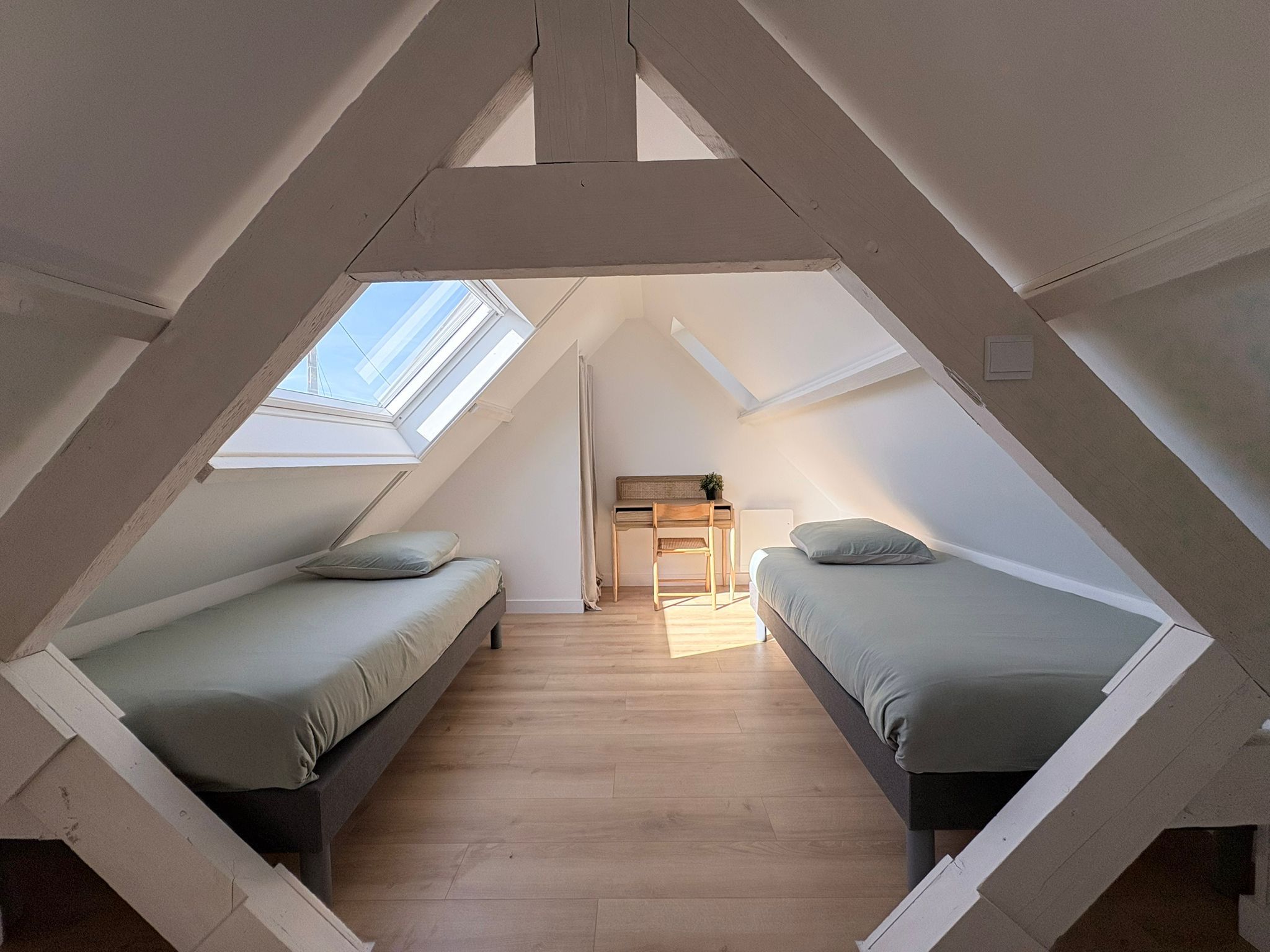 A triangular attic bedroom with two beds, a desk, and a skylight.