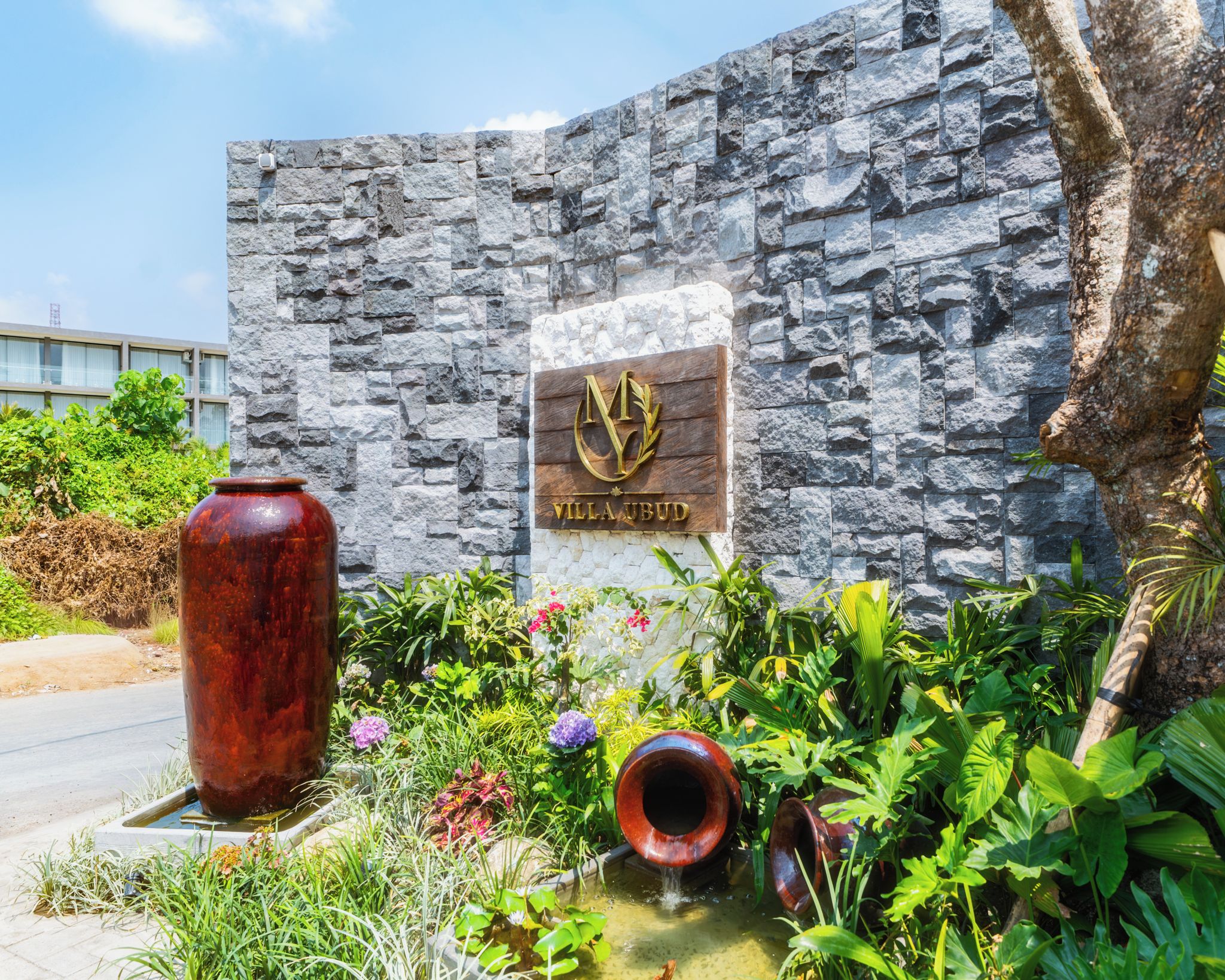 Un muro de piedra con una placa que dice 'VILLA UBUD' y un jarrón grande.