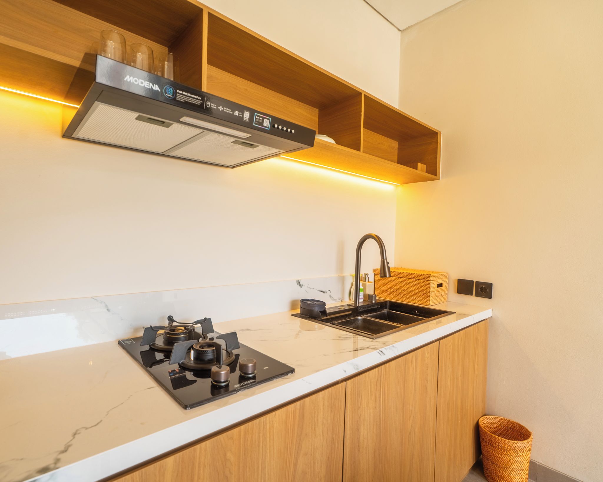 Una cocina moderna con estufa integrada, un lavamanos, armarios de madera y una campana extractora de acero inoxidable.