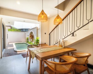Un comedor con una mesa y sillas de madera, una escalera y vistas a una piscina.