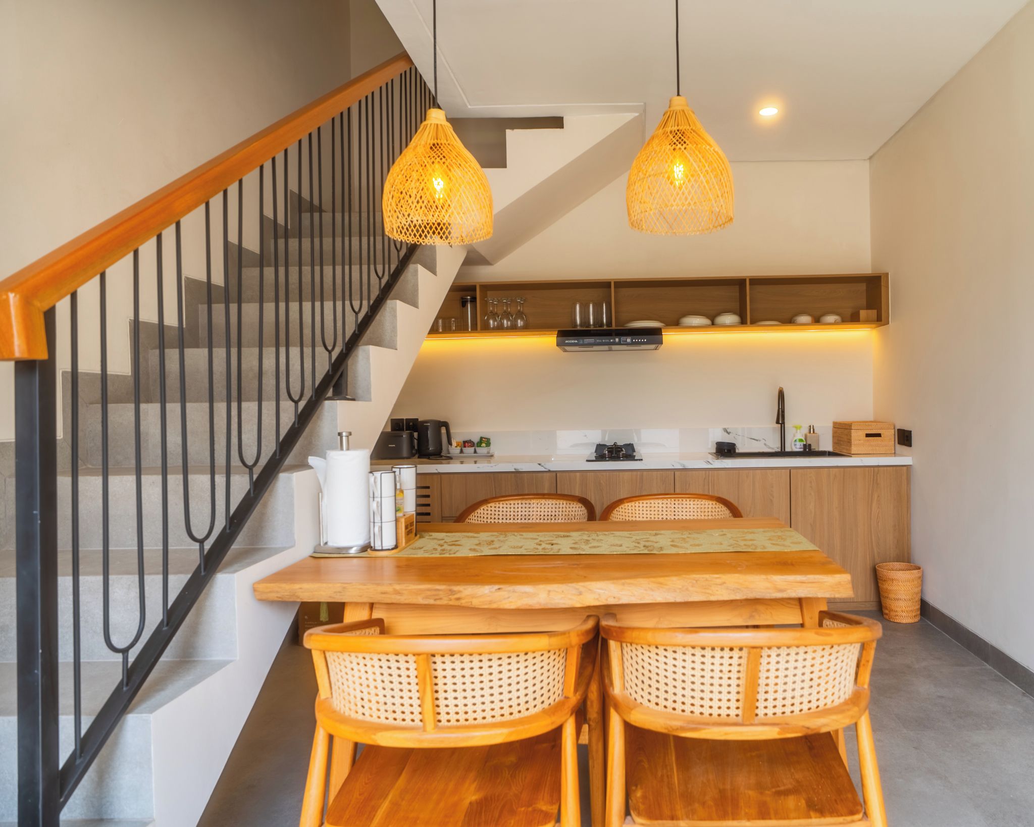 Una cocina moderna con una mesa de comedor de madera, sillas de mimbre e iluminación colgante.