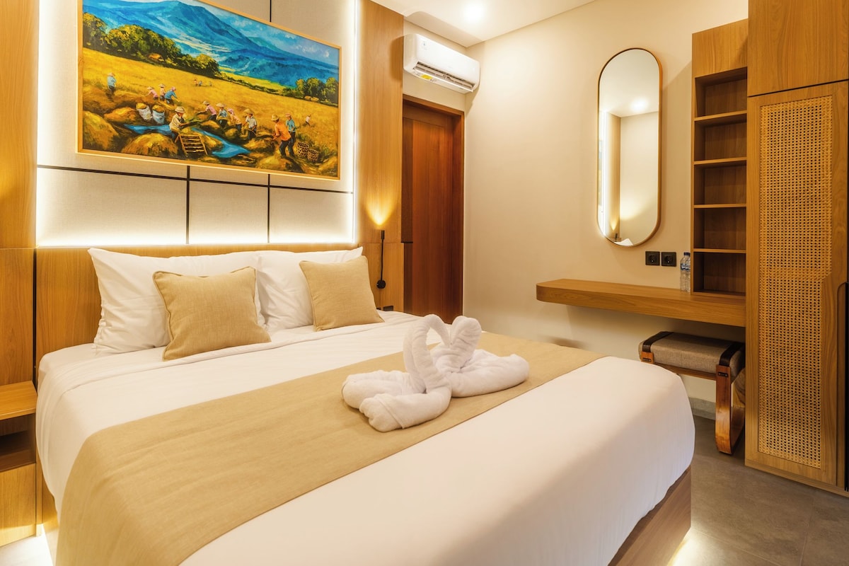 Habitación de hotel con una cama grande, un cuadro en la pared, un espejo y un armario de madera.