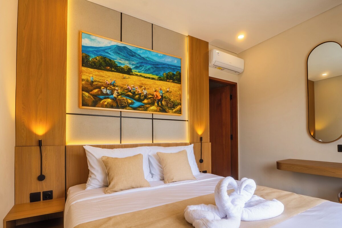 Una habitación de hotel con una cama, un cuadro, aire acondicionado de pared y un espejo.