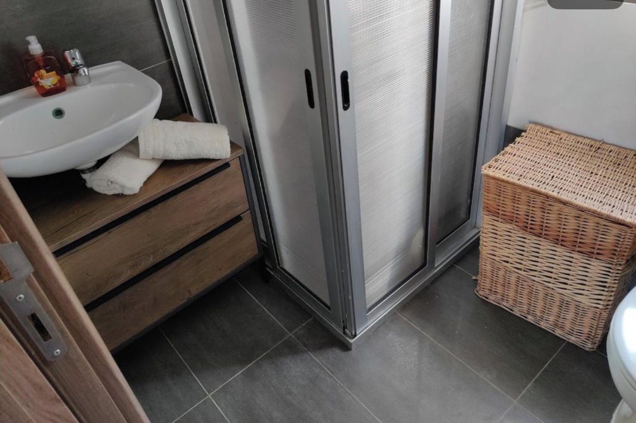 A bathroom with a white sink, a wooden vanity, a stainless steel shower enclosure, and a wicker basket.