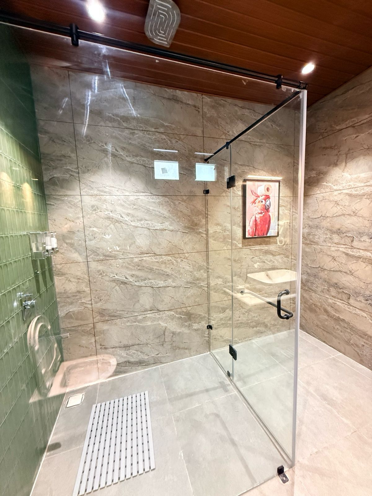 A modern bathroom with a glass shower enclosure, marble walls, and a green tiled shower area.