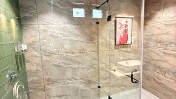 A modern bathroom with a glass shower enclosure, marble walls, and a green tiled shower area.
